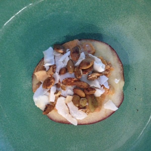 Sliced apple with peanut butter, pumpkin seeds, and coconut flakes